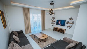 A modern living room with a sofa set, a coffee table, and a TV mounted on the wall. - Luxury 3BR Apartment with Mountain View, AC & Pool – Maşukiye (Kocaeli)