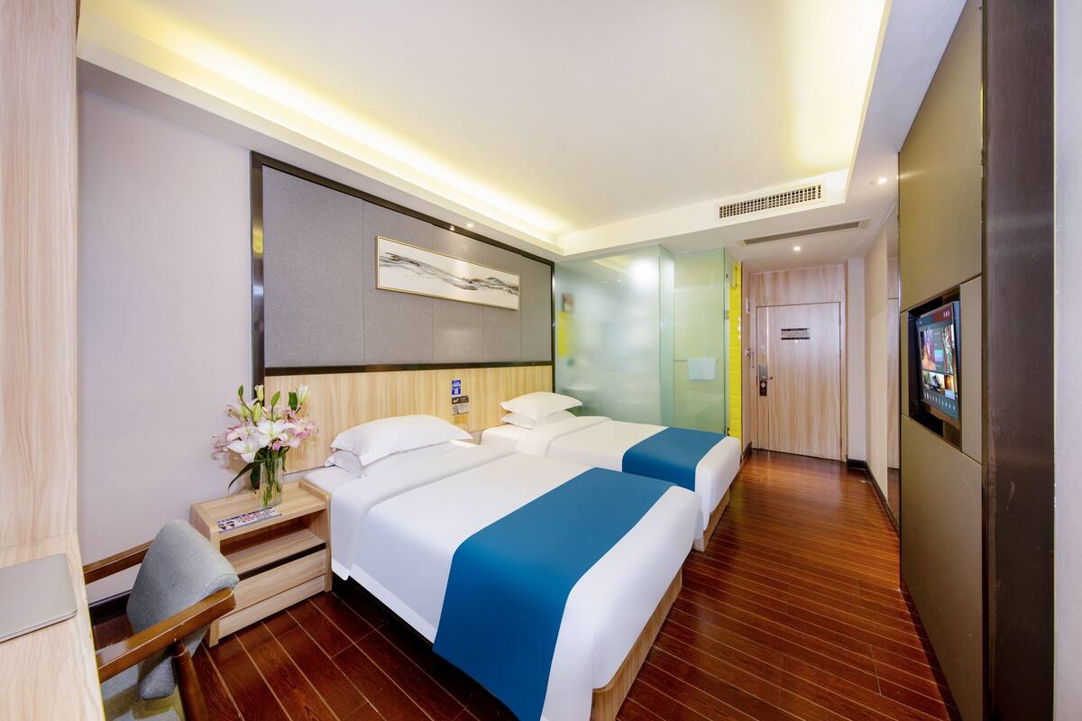 Habitación de hotel con dos camas, un escritorio con silla, un televisor y un jarrón con flores.
