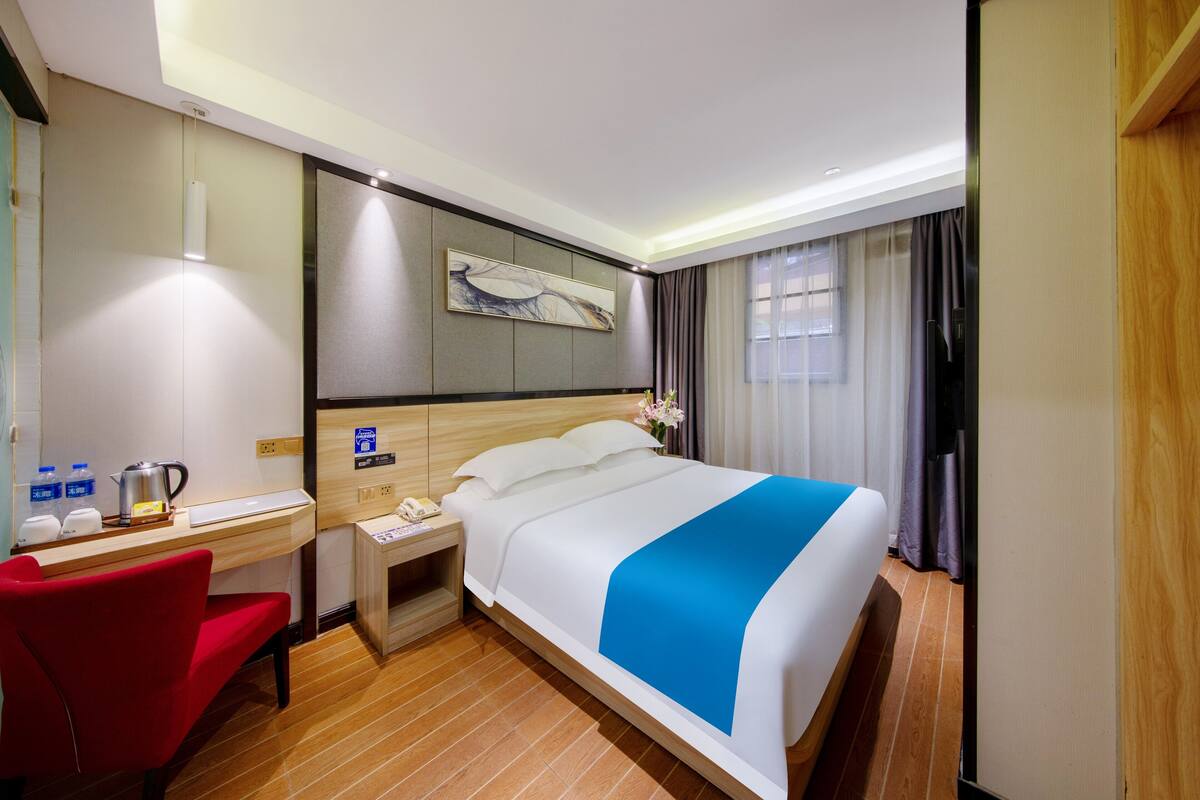Habitación de hotel con cama, escritorio, silla, mesita de noche y una obra de arte en la pared.