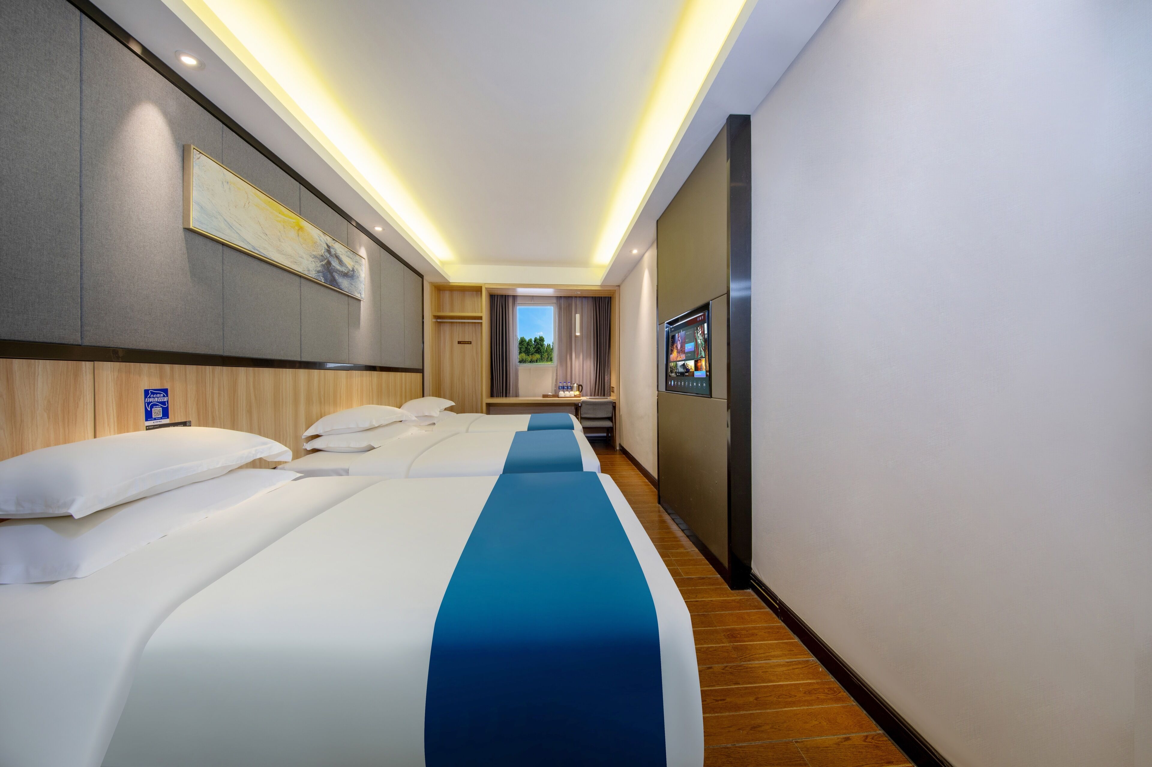 Habitación de hotel con tres camas, televisión y vistas al exterior.