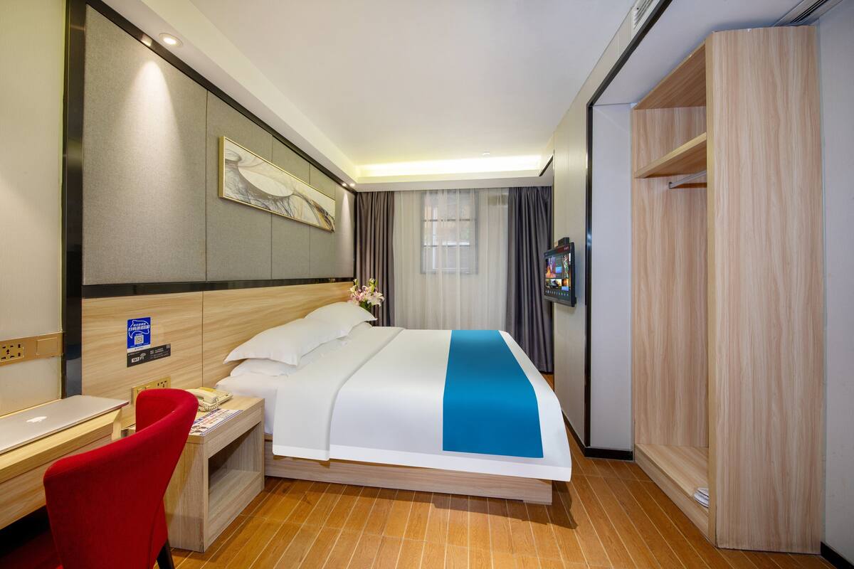 Una habitación de hotel con cama, escritorio, silla, armario y espejo.