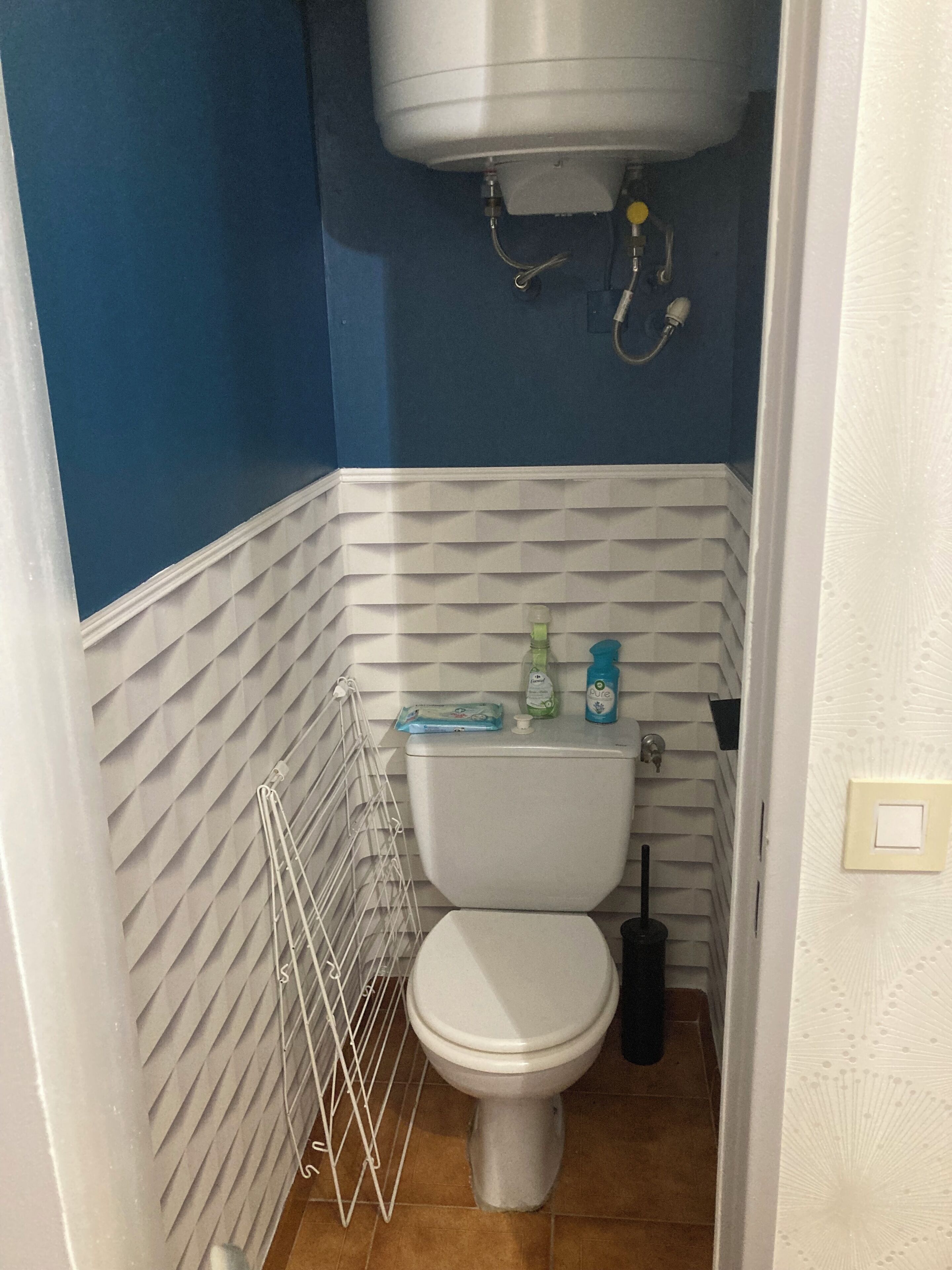 A small bathroom with a white toilet, a white towel rack, and a blue wall.