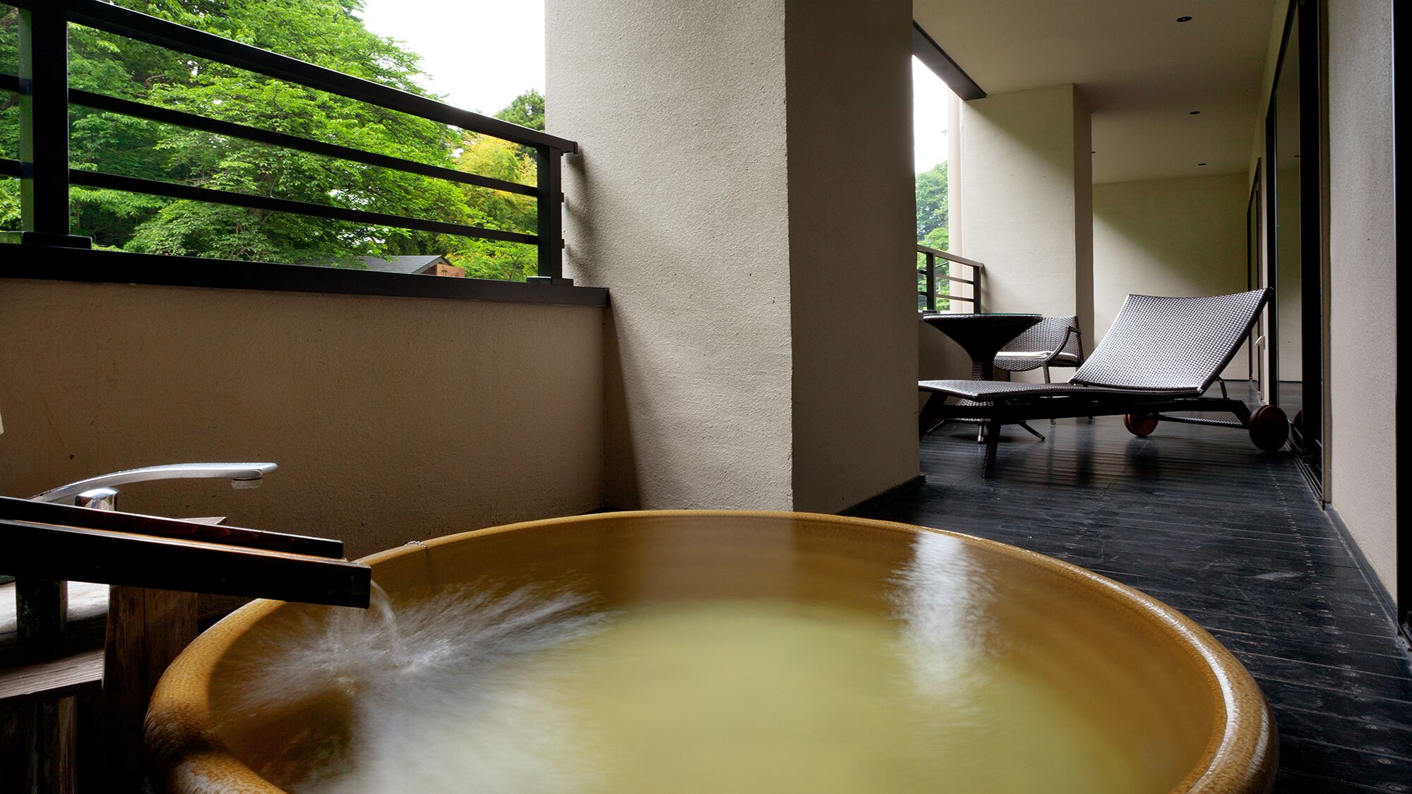 Ein Wellnessbereich mit einer großen Holzwanne, einem Sessel und einem Tisch.