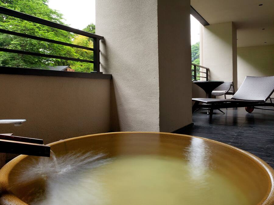 Ein Wellnessbereich mit einer großen Holzwanne, einem Sessel und einem Tisch.