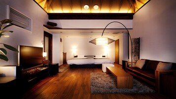 A modern hotel room with a wooden floor, a large bed, a sofa, a TV, and a ceiling light fixture.
