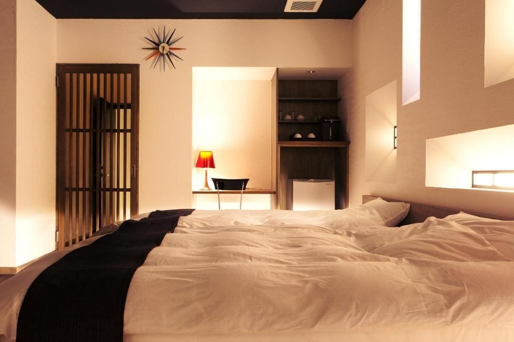 Un dormitorio con una cama grande, un escritorio con silla, un armario y una lámpara fijada a la pared.