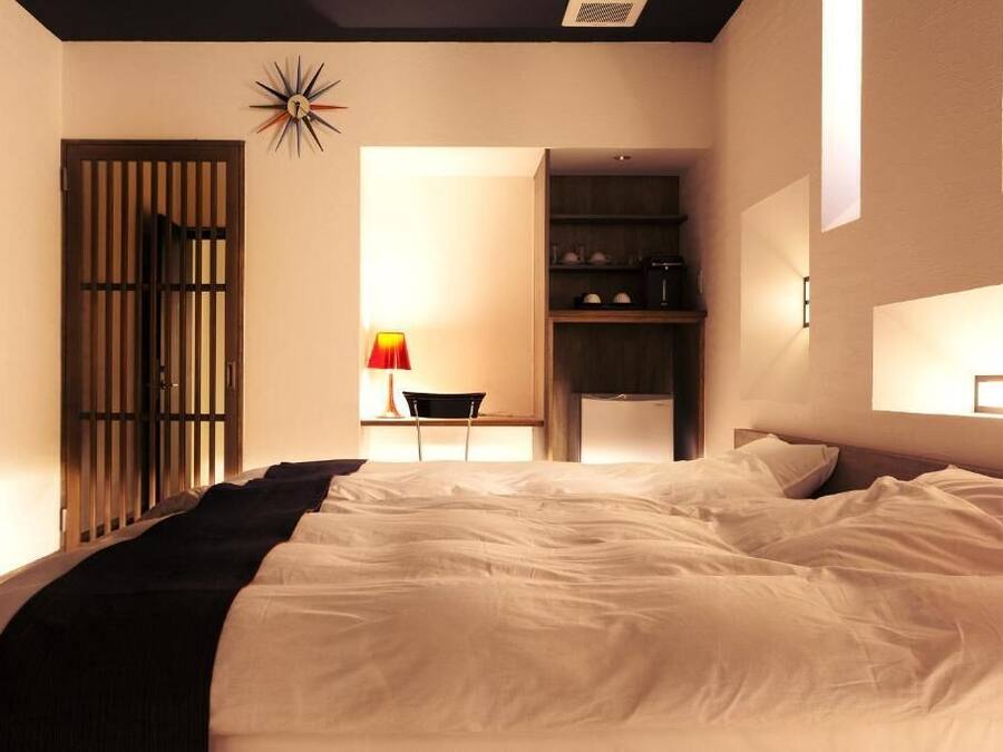 Un dormitorio con una cama grande, un escritorio con silla, un armario y una lámpara fijada a la pared.