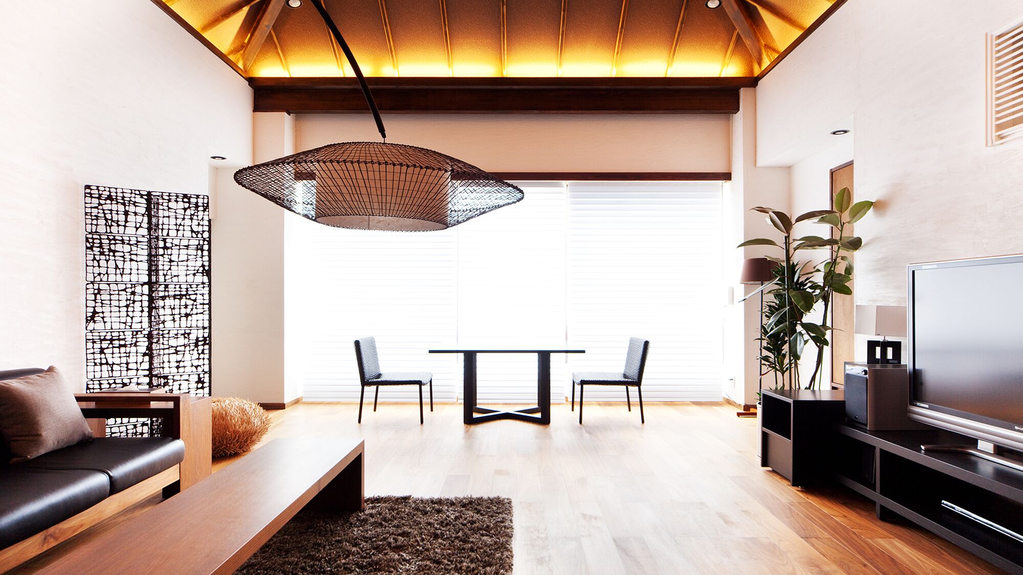 Una sala de estar moderna con un sofá, una mesa de centro, una mesa de comedor con sillas, un televisor y una planta grande.