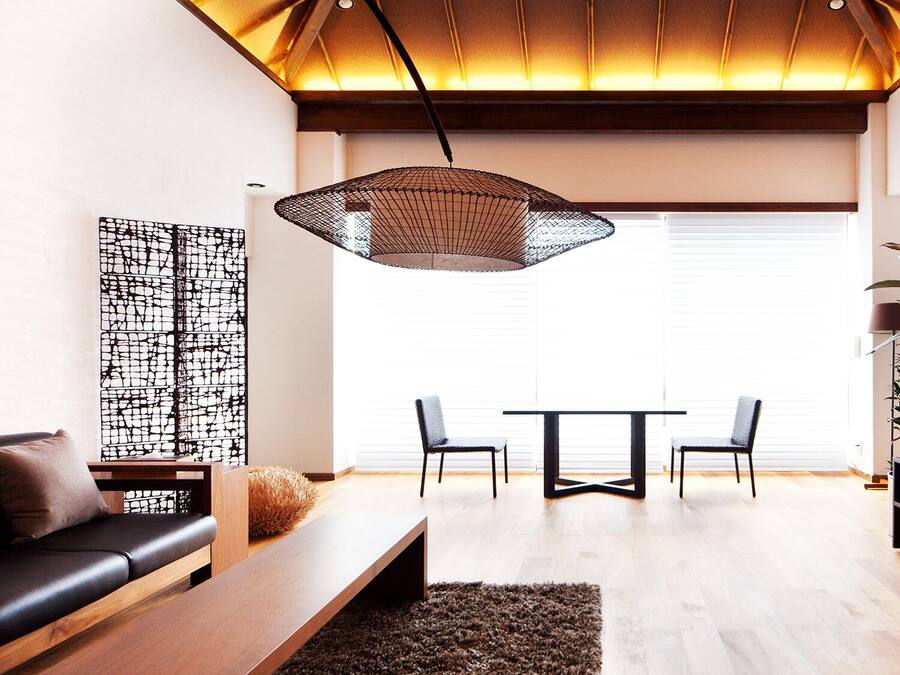 Una sala de estar moderna con un sofá, una mesa de centro, una mesa de comedor con sillas, un televisor y una planta grande.