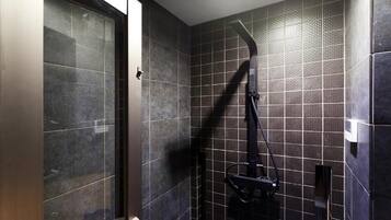 A bathroom with dark tiled walls, a shower area, and a glass door.