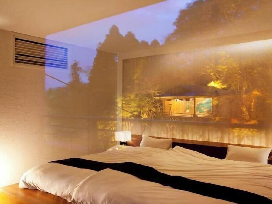 A bedroom with a bed, a nightstand, and a wall-mounted projector displaying a scenic view.