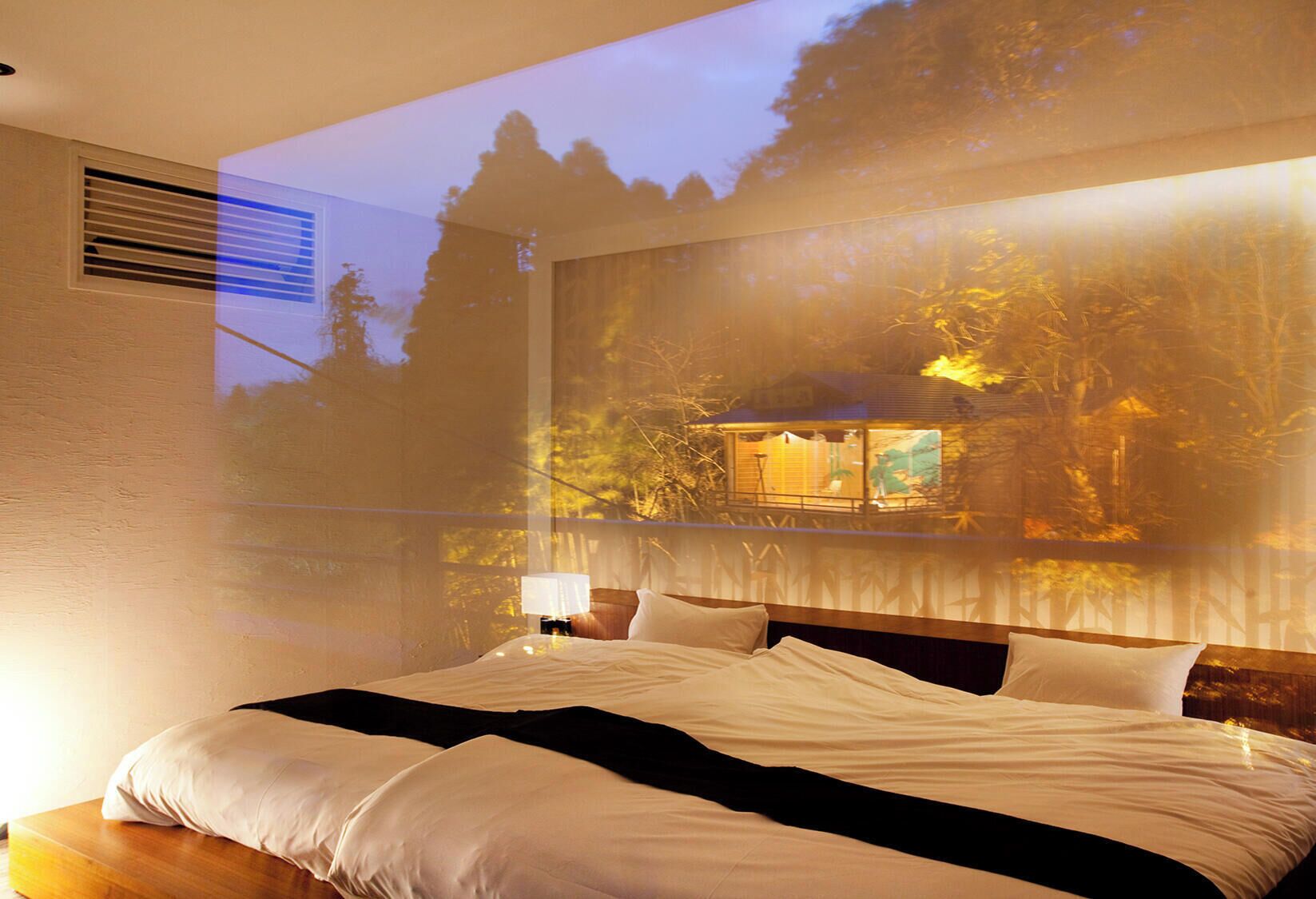 Un dormitorio con cama, mesita de noche y un ventanal grande.