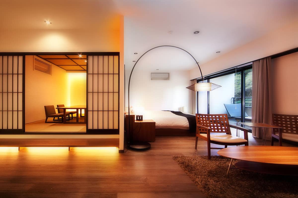 A modern interior with a wooden floor, a dining area with a table and chairs, a sofa, a lamp, and a view through a shoji screen.
