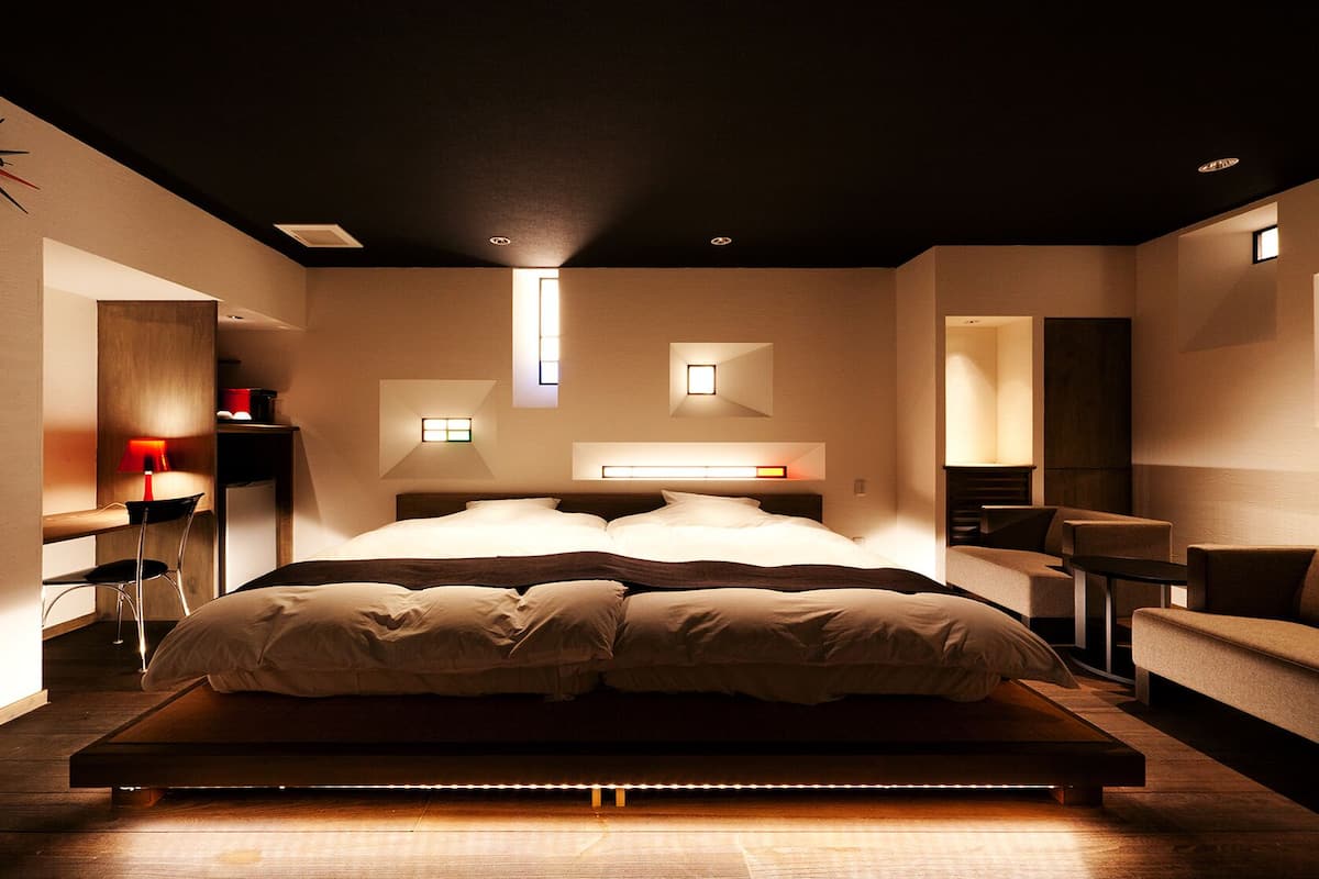 A modern bedroom with a large bed, bedside tables, a desk, and a sofa.