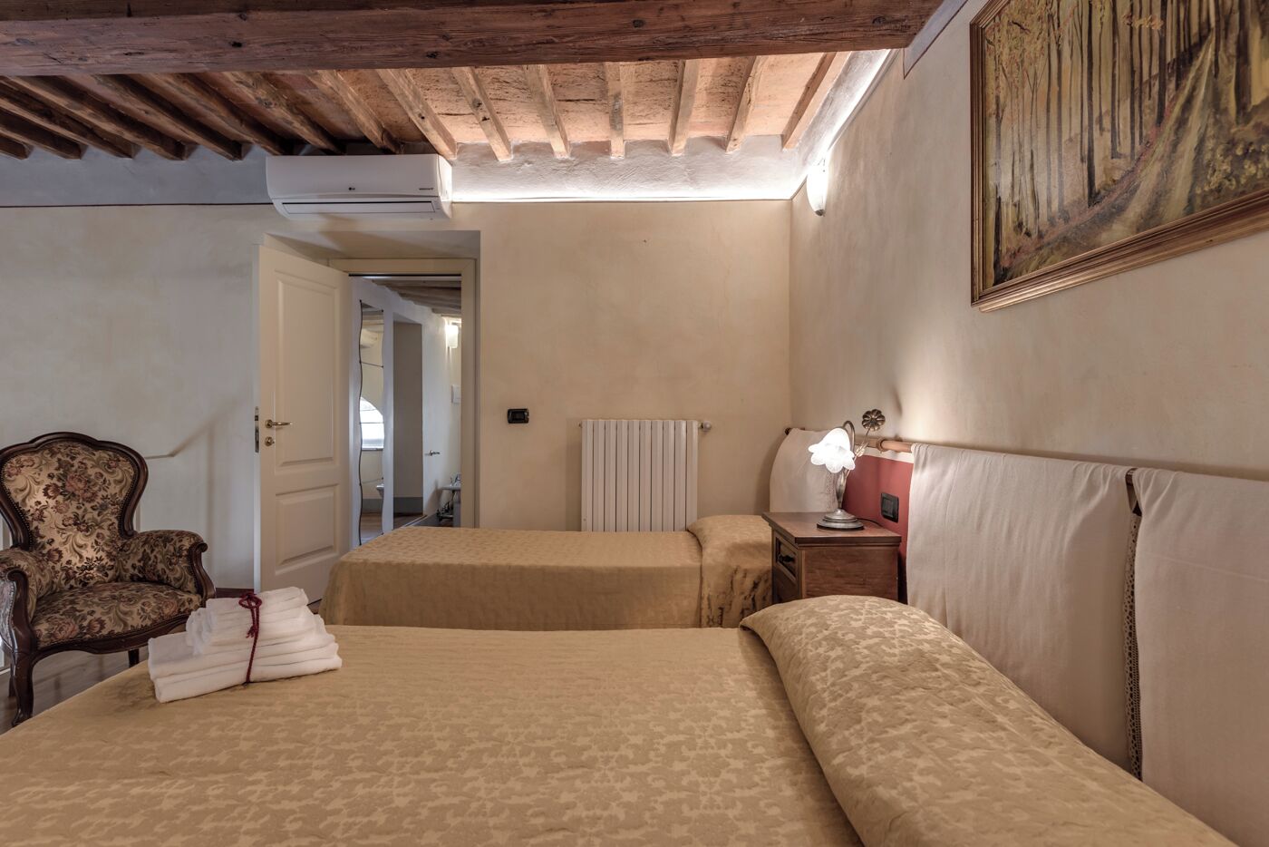 A room with two beds, a chair, a radiator, and a painting on the wall.