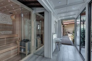 A modern interior with a glass door leading to a wooden sauna area, a tiled floor, and a view of a garden outside. - RESIDENCE LE GAGLIARDE Residence vacation home (Arezzo)