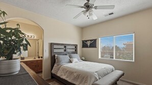 A bedroom with a bed, a ceiling fan, a window with blinds, a potted plant, and a wooden headboard. - Indulge in this beautiful New Mexico home located in Southwest Albuquerque (Albuquerque)