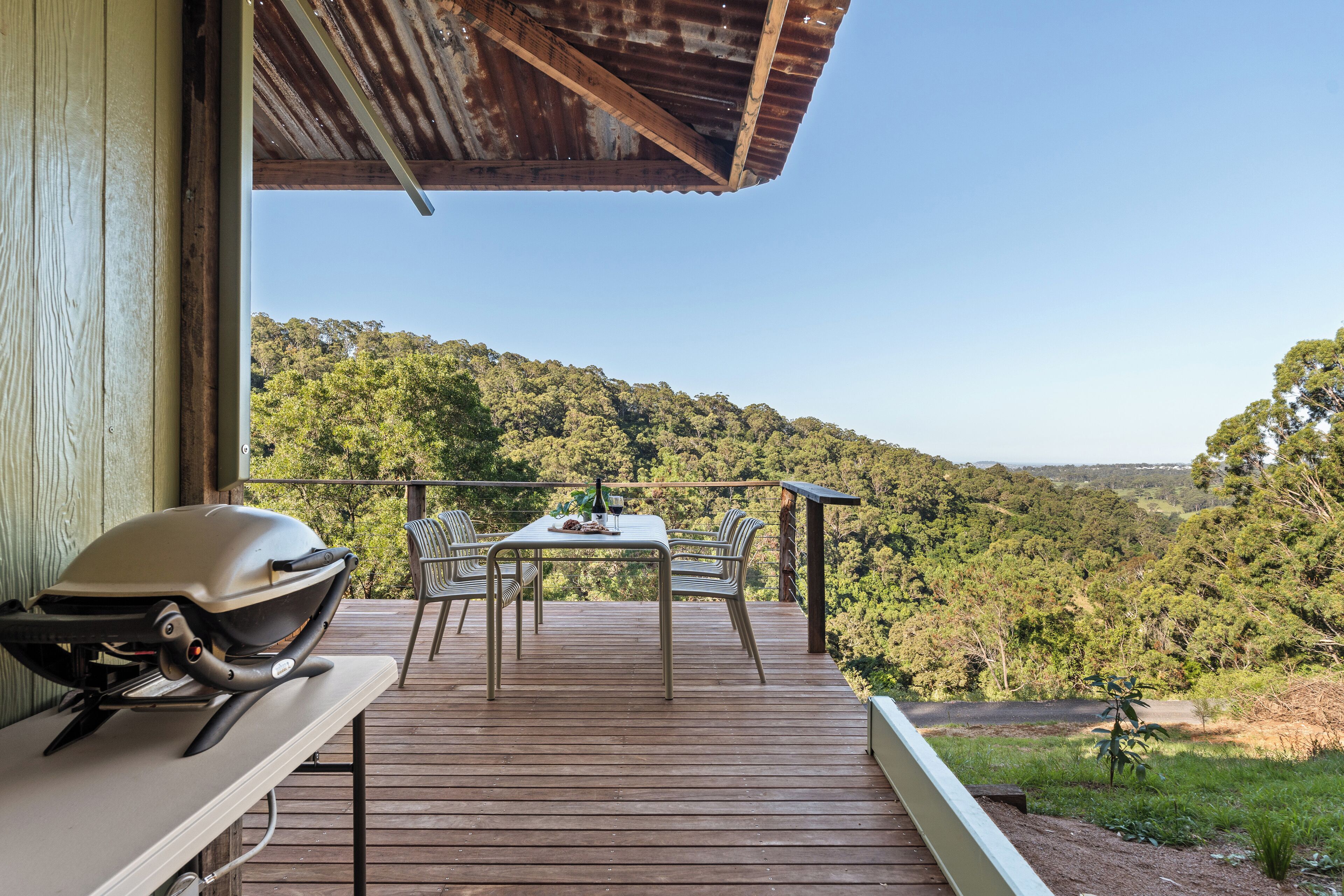 A wooden deck with a table and chairs overlooking a forested hillside.