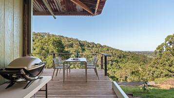 A wooden deck with a table and chairs overlooking a forested hillside.