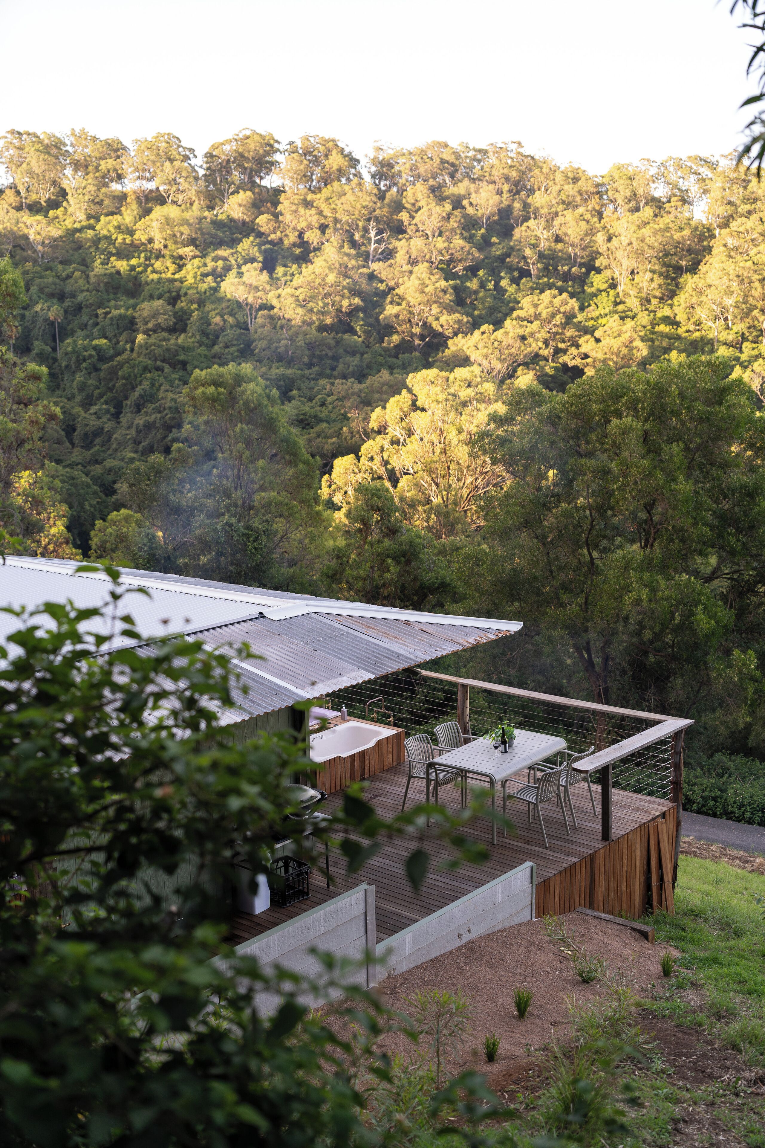 A wooden deck with a table and chairs, surrounded by a fence, overlooking a forested area.