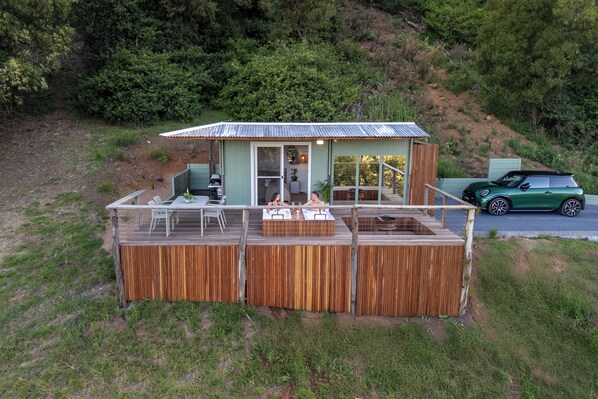 A small wooden cabin with a deck, a covered porch, and a car parked nearby.