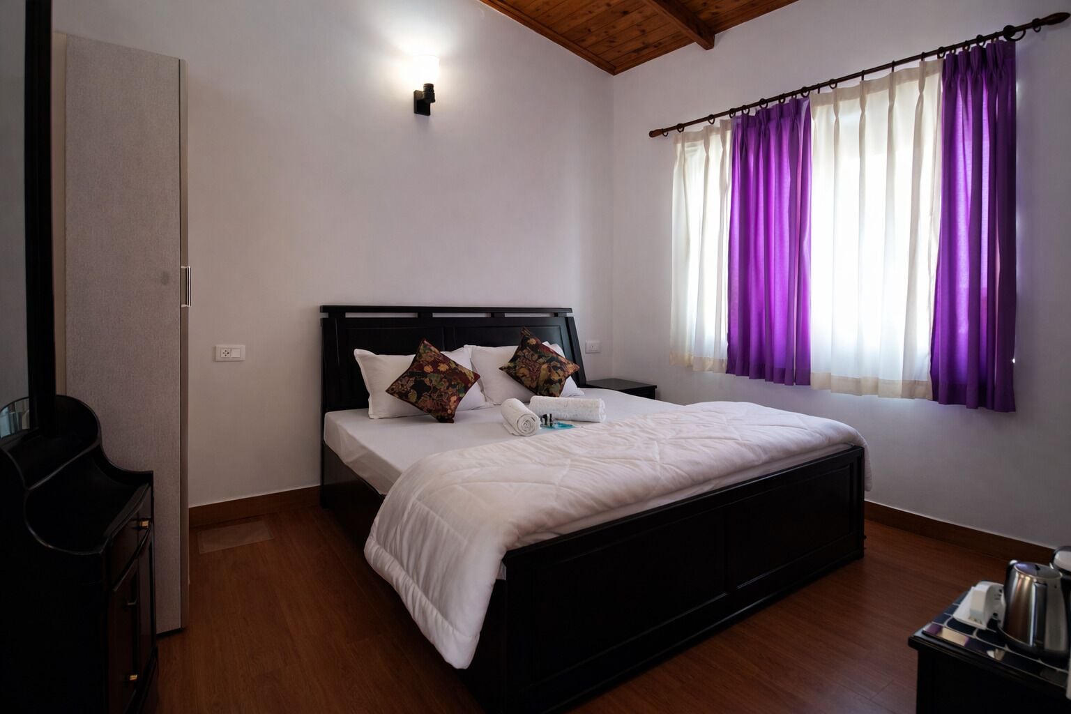 A bedroom with a bed, pillows, a nightstand, a window with curtains, and a ceiling light.