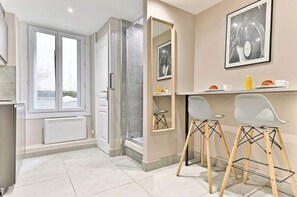 Un baño moderno con ducha, inodoro y lavamanos. Hay una ventana que proporciona luz natural y un cuadro en la pared.