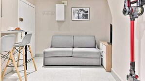 En moderne stue med en grå sofa, et spisebord med stole, et hvidt skab og et rødt rengøringsværktøj på væggen.