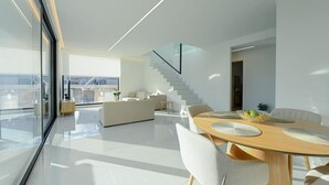 A modern living space with a dining area, a staircase, and a view through large windows. - Executive 3-Bedroom Deluxe Stay (Heraklion)