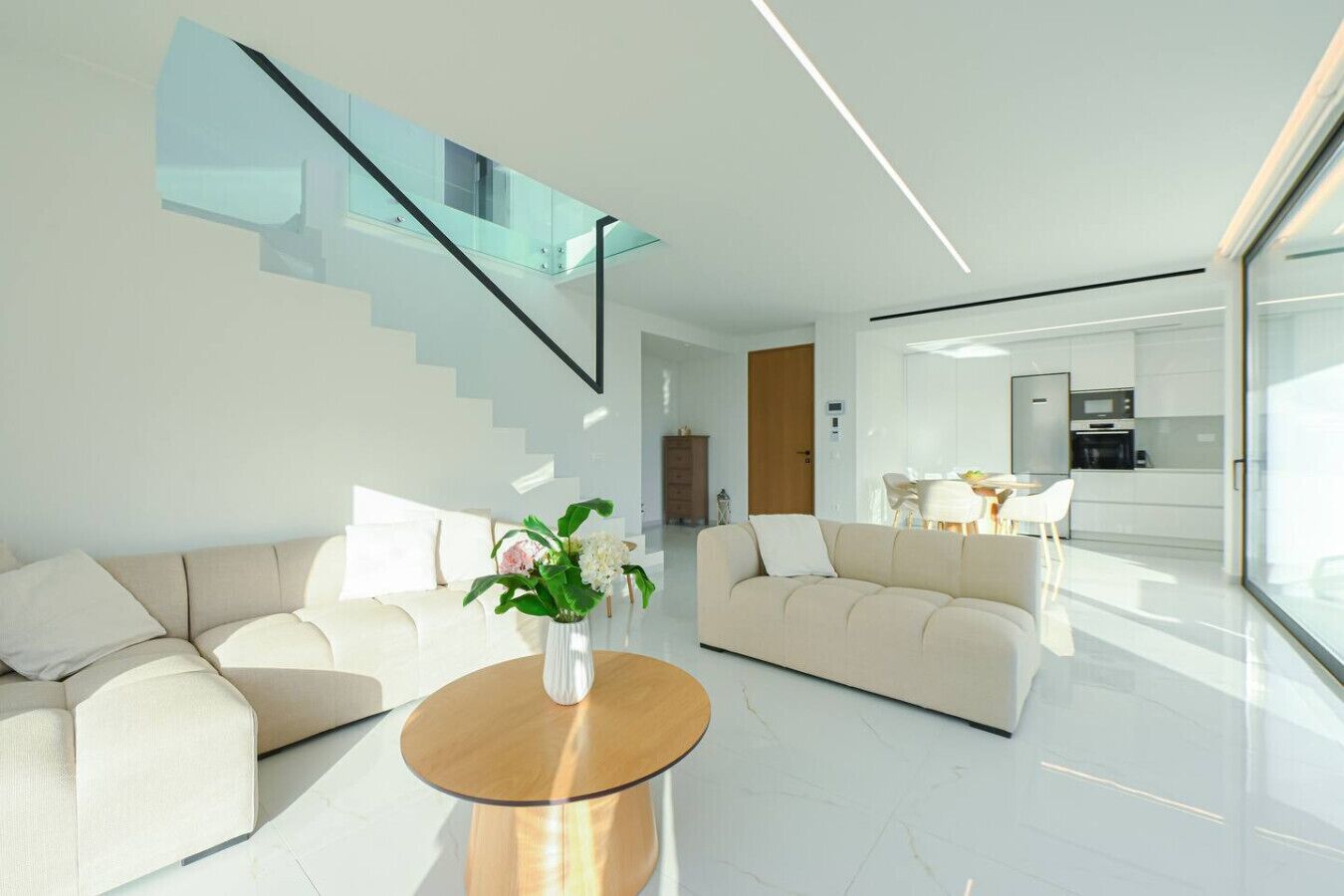 Un salon moderne avec deux canapés, une table basse et un escalier doté de rampes en verre.