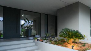 A modern house with a flat roof, a large potted plant, and a small garden area with rocks and plants. - Executive 3-Bedroom Deluxe Stay (Heraklion)