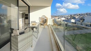 A balcony with wicker furniture, a glass table, and a view of a cityscape. - Executive 3-Bedroom Deluxe Stay (Heraklion)