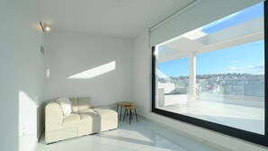 A modern, minimalist living room with a large window offering a city view. - Executive 3-Bedroom Deluxe Stay (Heraklion)
