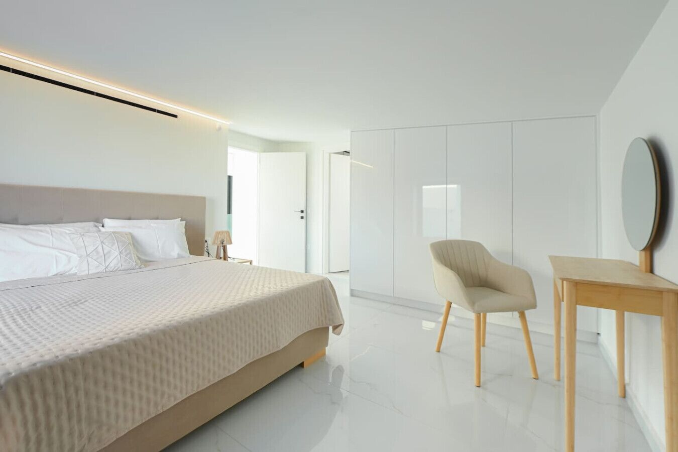 Un dormitorio moderno con una cama grande, una silla, una mesita y un espejo en la pared.