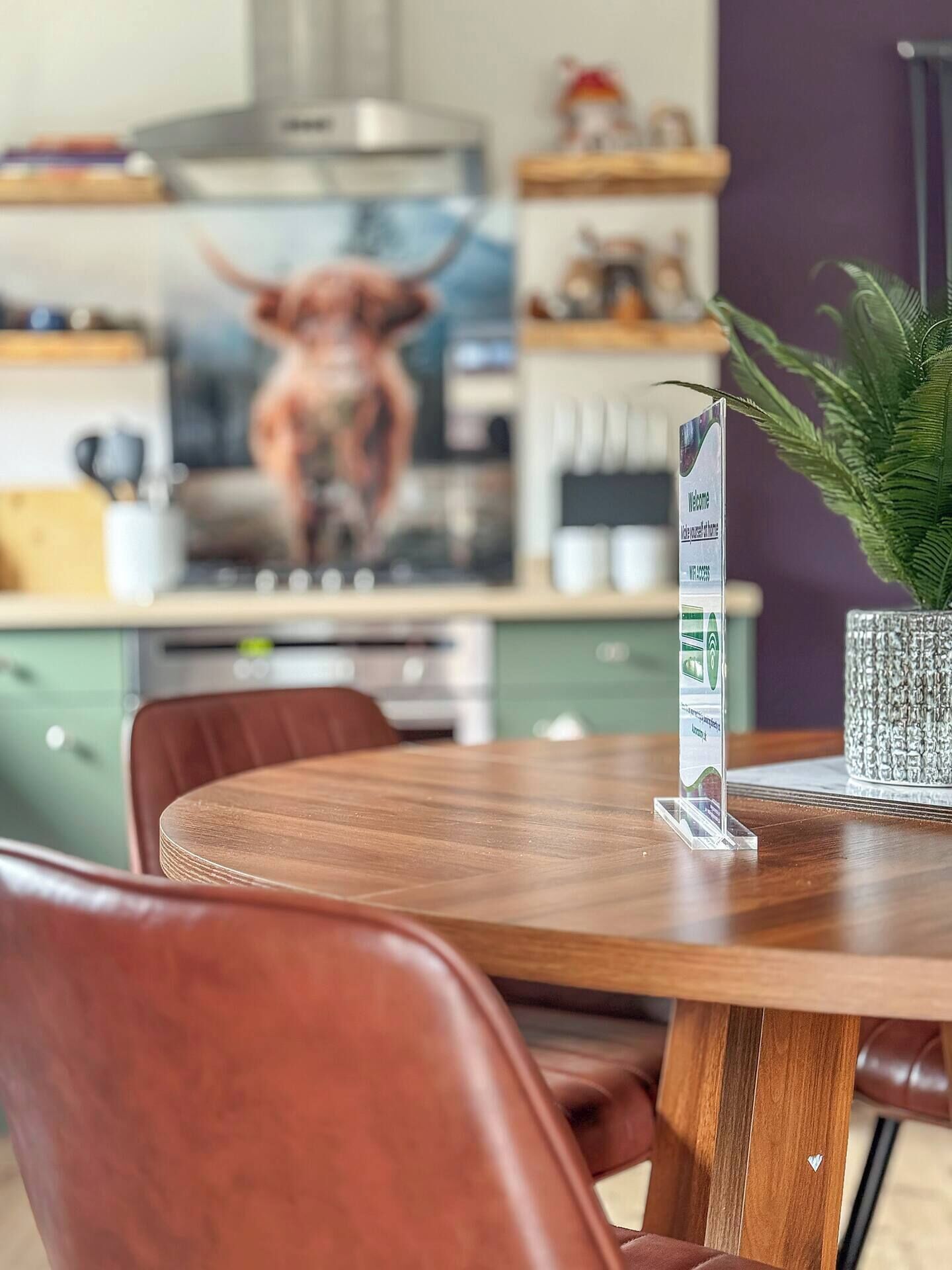 Een eetgedeelte met een houten tafel en stoelen, een potplant en een keuken op de achtergrond met een stierbeeld.