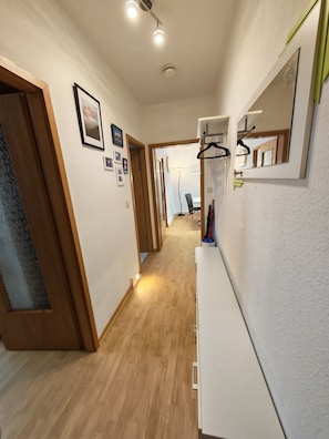A hallway with wooden flooring, a coat rack, and framed pictures on the wall.