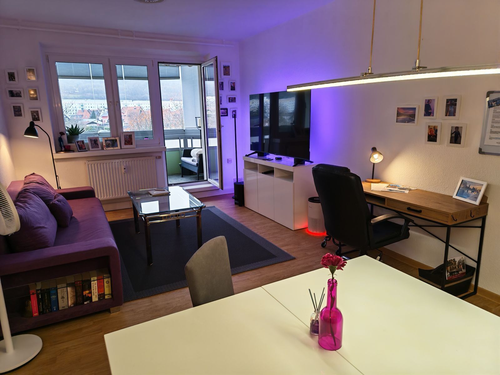 A modern living room with a sofa, a coffee table, a TV, and a desk area with a computer.