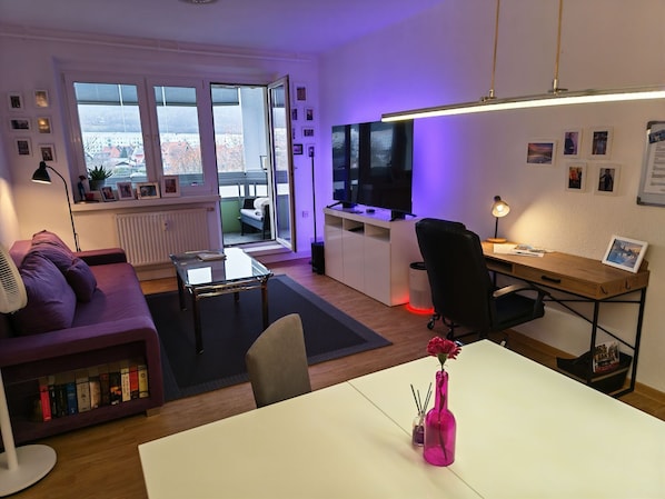 A modern living room with a sofa, a coffee table, a TV, and a desk area with a computer.
