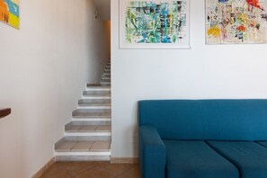 A staircase leading to a landing, a blue sofa, and abstract art on the wall. - GuestHost - The house is located in the heart of the residential and tourist district of Porto Corallo, a hamlet of the municipality of Villaputzu, on the south-eastern coast of Sardinia. The area is known for its natural beauty, tranquility and the pres (Porto Tramatzu)