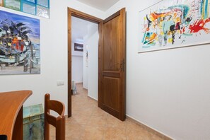 A hallway with a wooden door, a dining table with chairs, and two paintings on the walls. - GuestHost - The house is located in the heart of the residential and tourist district of Porto Corallo, a hamlet of the municipality of Villaputzu, on the south-eastern coast of Sardinia. The area is known for its natural beauty, tranquility and the pres (Porto Tramatzu)