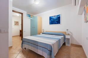 A bedroom with a bed, bedside table, and a painting on the wall. - GuestHost - The house is located in the heart of the residential and tourist district of Porto Corallo, a hamlet of the municipality of Villaputzu, on the south-eastern coast of Sardinia. The area is known for its natural beauty, tranquility and the pres (Porto Tramatzu)