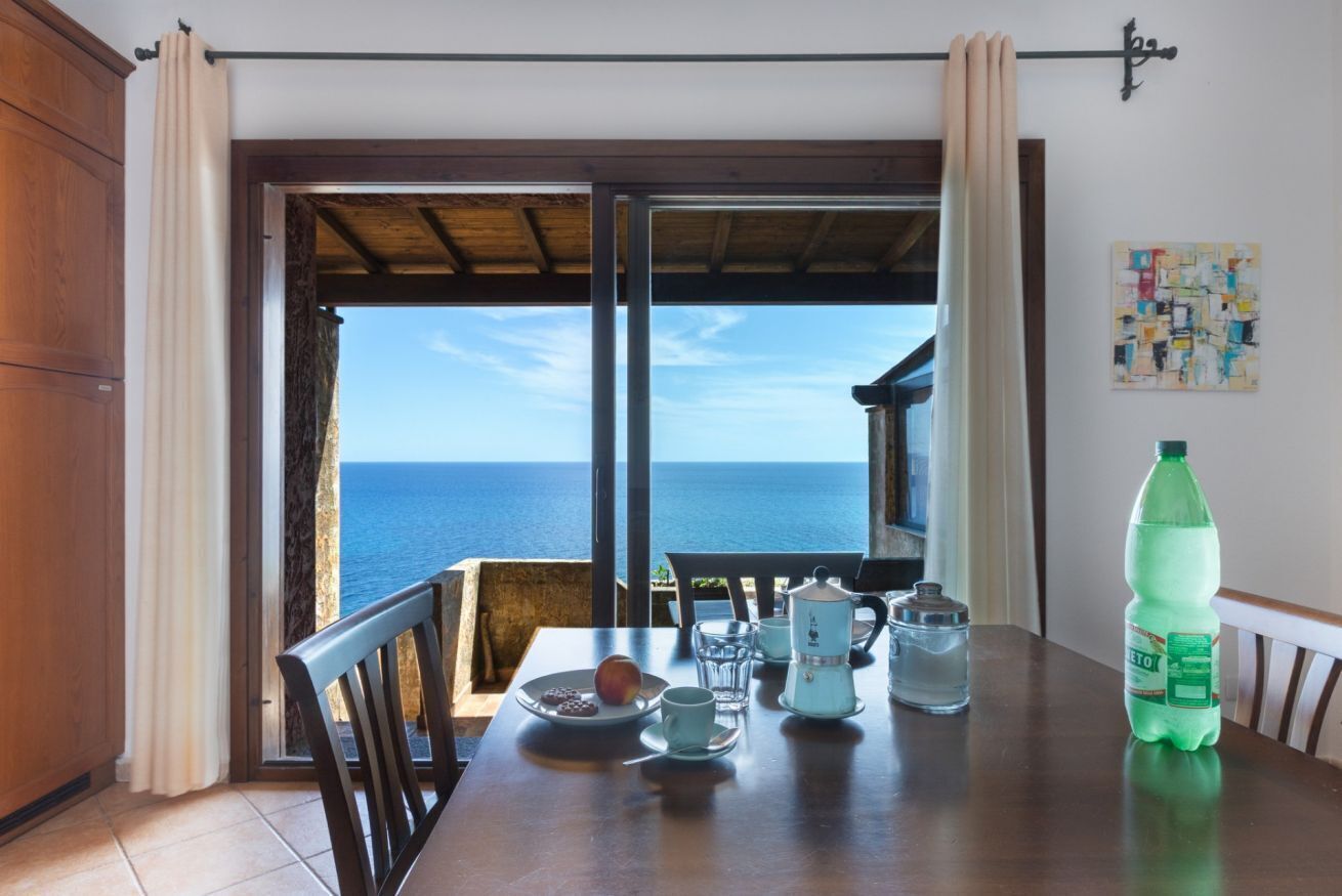 A dining area with a table set for two, a view of the sea, and a bottle of water on the table.