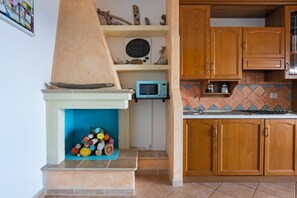A kitchen with wooden cabinets, a microwave, and a fireplace with logs. - GuestHost - The house is located in the heart of the residential and tourist district of Porto Corallo, a hamlet of the municipality of Villaputzu, on the south-eastern coast of Sardinia. The area is known for its natural beauty, tranquility and the pres (Porto Tramatzu)