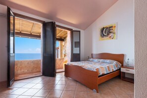 A bedroom with a bed, a nightstand, a painting, and a view through an open door. - GuestHost - The house is located in the heart of the residential and tourist district of Porto Corallo, a hamlet of the municipality of Villaputzu, on the south-eastern coast of Sardinia. The area is known for its natural beauty, tranquility and the pres (Porto Tramatzu)