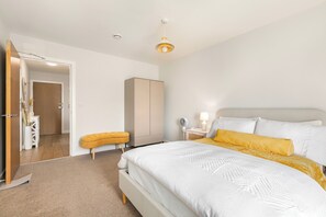 A bedroom with a bed, a wardrobe, a bedside table with a lamp, and a door leading to another room. - Apartment - Sleeps 3 - Royalvictoriastation 5mins (London)