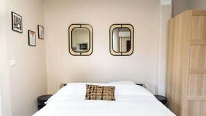 Een slaapkamer met een bed, twee nachtkastjes, een houten kledingkast en twee spiegels aan de muur.