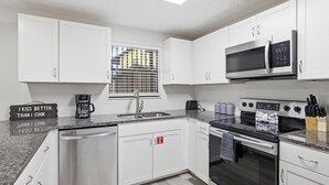 Una cocina moderna con armarios blancos, un lavavajillas de acero inoxidable, un microondas, un horno y una cafetera.