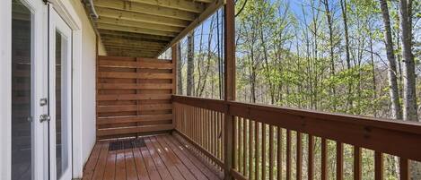 A wooden deck with a railing, a door with a screen, and a view of trees.