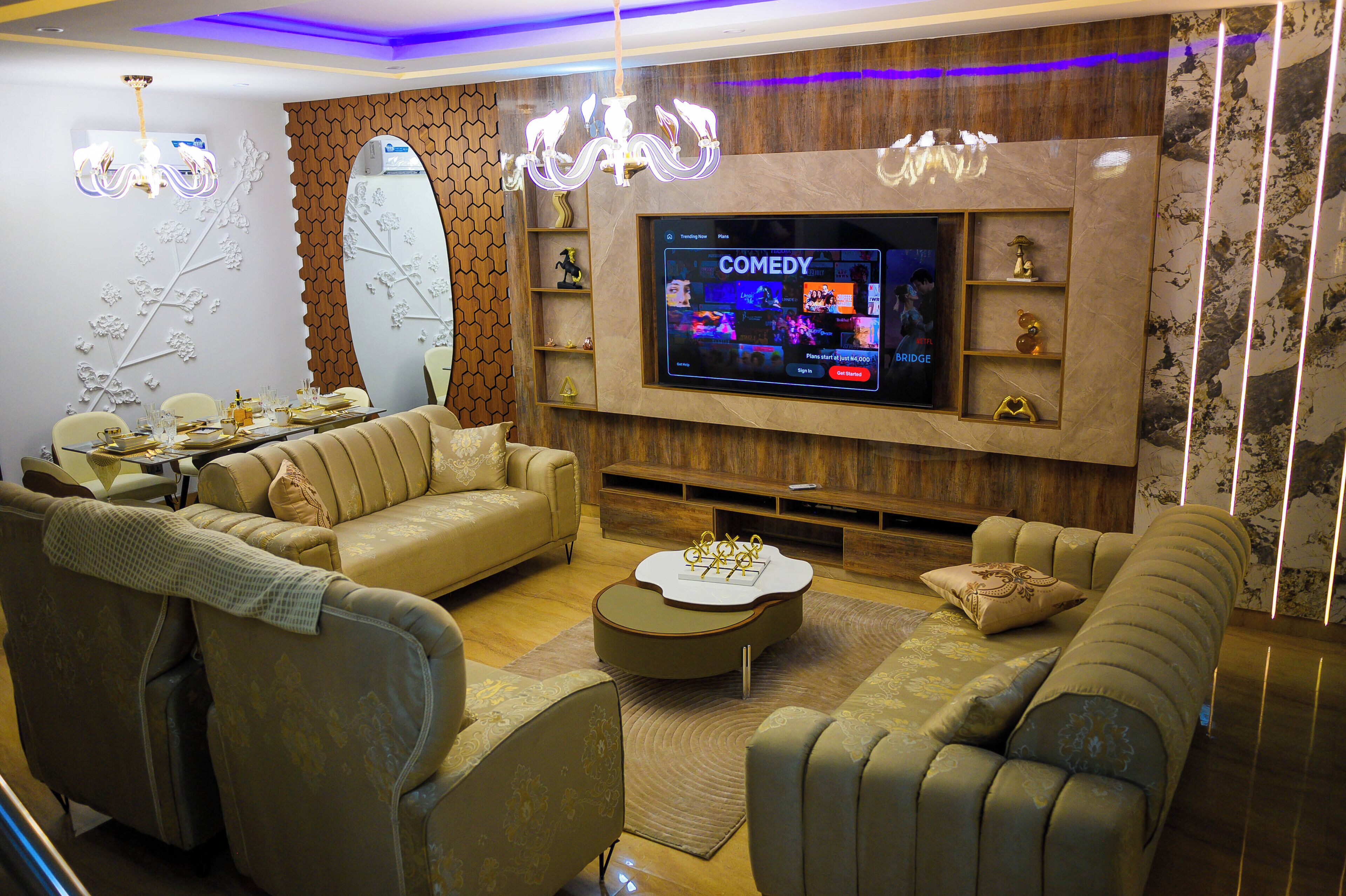 A modern living room with a large flat-screen TV, comfortable sofas, a coffee table, and decorative wall art.