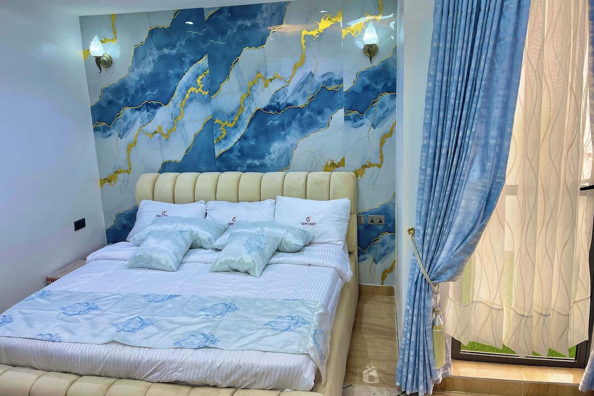 A bedroom with a bed, a wall with a marble-like design, and a window with curtains.